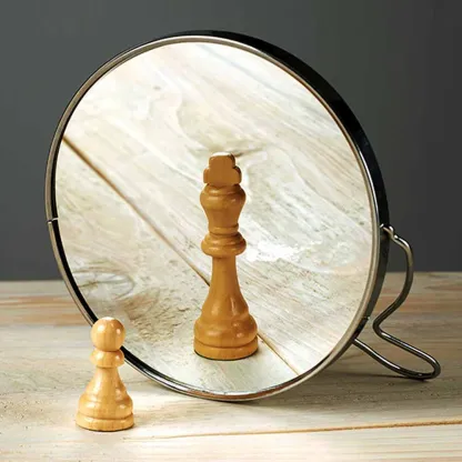 A small wooden chess pawn looking into a mirror and seeing the reflection of a king piece, symbolizing self-confidence, ambition, and inner potential.